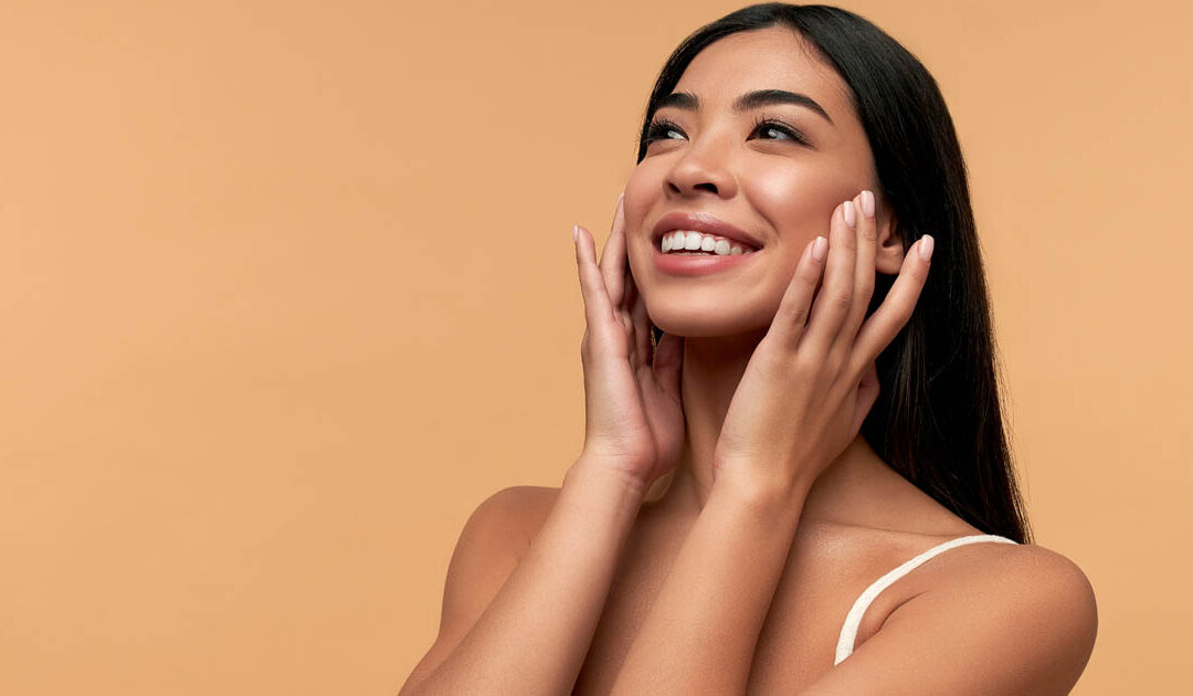woman touching her face and smiling, realizing the benefits of waxing