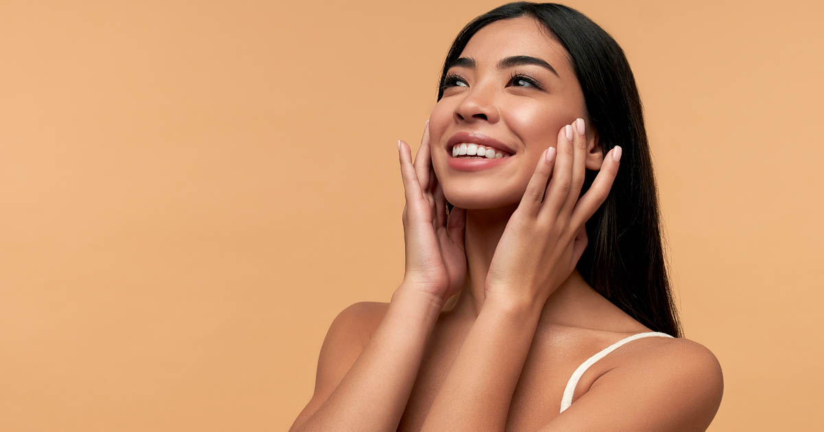 woman touching her face and smiling, realizing the benefits of waxing